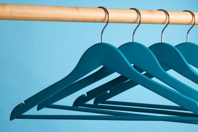 Bright clothes hangers on wooden rail against light blue background, closeup