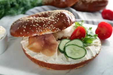 Delicious bagel with cream cheese, jamon, cucumber, tomato and parsley on white board, closeup