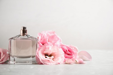 Bottle of perfume with fresh flowers on light background, space for text