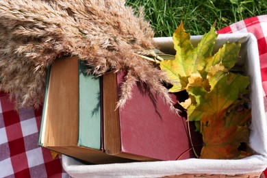 Books, maple leaves and reed in wicker basket outdoors. Autumn atmosphere