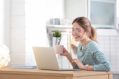 Image of Young woman with cup of coffee working on laptop at home