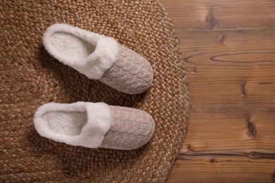 Photo of Pair of warm stylish slippers and wicker mat on wooden floor, flat lay. Space for text