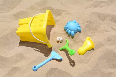 Photo of Bright plastic bucket, rake and shovel on sand. Beach toys