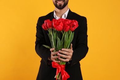 Happy man with red tulip bouquet on yellow background, closeup. 8th of March celebration