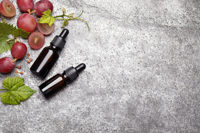 Bottles of natural grape seed oil on grey table, flat lay with space for text. Organic cosmetic