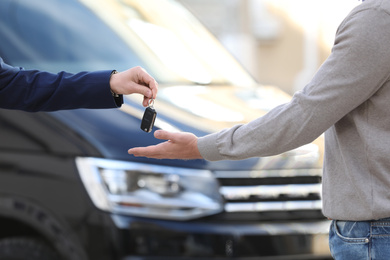 Photo of Salesman giving key to customer in modern auto dealership, closeup. Buying new car
