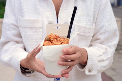 Photo of Woman holding paper box of takeaway noodles with fork outdoors, closeup. Street food