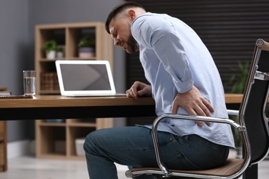 Man suffering from back pain while working with laptop in office. Symptom of poor posture