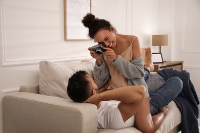 Beautiful African-American woman taking picture of her boyfriend on sofa at home