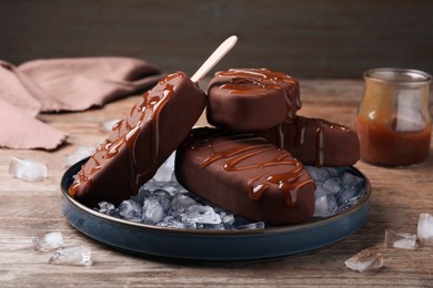 Delicious glazed ice cream bars and ice cubes on wooden table