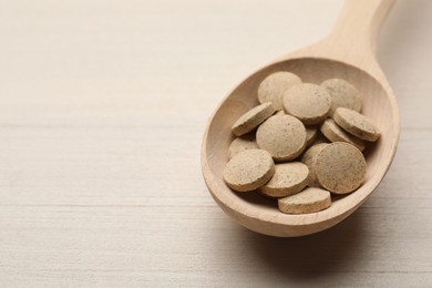 Photo of Spoon with dietary supplement pills on white wooden table, closeup. Space for text