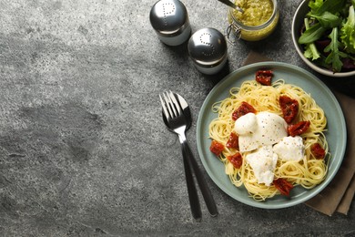 Delicious spaghetti with burrata cheese and sun dried tomatoes served on grey table, flat lay. Space for text