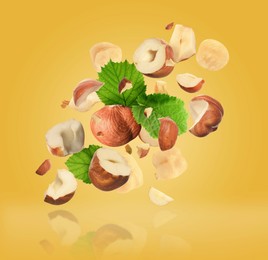 Pieces of tasty hazelnuts falling on yellow background