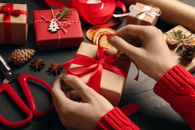 Woman decorating gift box at black table, closeup. Christmas present