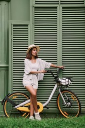 Beautiful young woman with bicycle near green wall outdoors