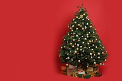 Beautifully decorated Christmas tree and many gift boxes on red background, space for text