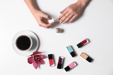 Woman applying nail polish near coffee and bottles on white background, top view