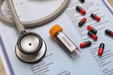 Test tube with blood sample, stethoscope, pills and medical form on table, closeup. Anemia concept