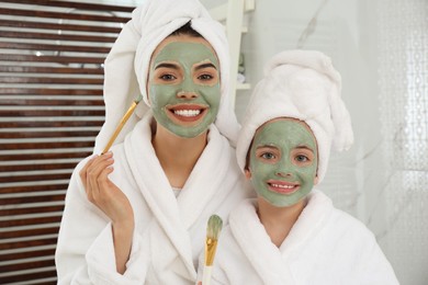 Young mother and her daughter with facial masks in bathroom