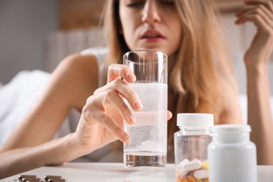 Woman taking medicine for hangover at home, focus on hand with glass