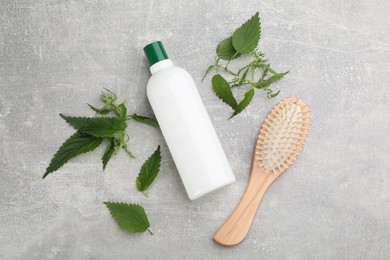 Stinging nettle, cosmetic product and brush on grey background, flat lay. Natural hair care