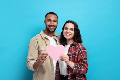 Photo of Lovely couple with pink paper heart on light blue background. Valentine's day celebration