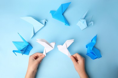 Photo of Origami art. Child holding paper birds on light blue background, closeup and top view