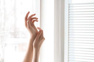 Young woman against window. Focus on hands moisturized with cream