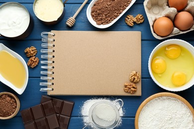 Photo of Blank recipe book surrounded by different ingredients on blue wooden table, flat lay. Space for text