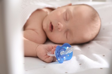 Cute little baby sleeping in bed, focus on hand with pacifier