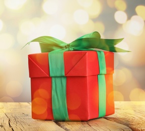 Christmas gift box on wooden table against blurred background, bokeh effect