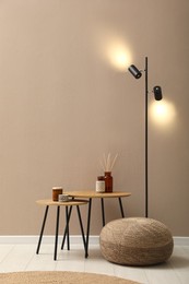 Photo of Knitted pouf, lamp and decor elements near beige wall indoors. Space for text