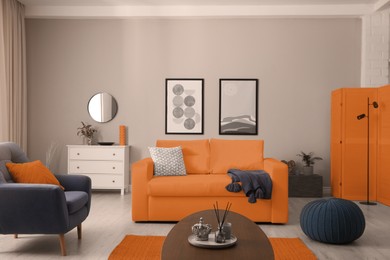 Image of Stylish living room interior with orange sofa, armchair and beautiful pictures