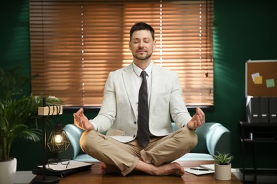 Calm businessman meditating on desk in office
