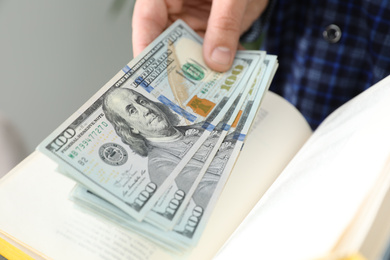 Man hiding dollar banknotes in book indoors, closeup. Money savings