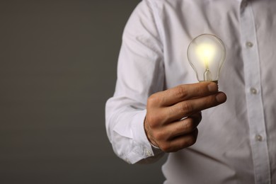 Glow up your ideas. Closeup view of man holding light bulb on grey background, space for text