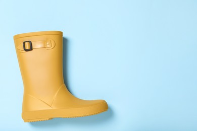 Yellow rubber boot on light blue background, top view. Space for text