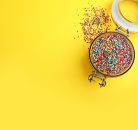 Colorful sprinkles in jar on yellow background, flat lay with space for text. Confectionery decor