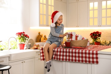 Cute little girl in Santa hat taking  gift from Christmas advent calendar on table at home