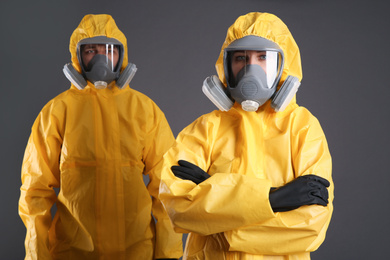Man and woman wearing chemical protective suits on grey background. Virus research