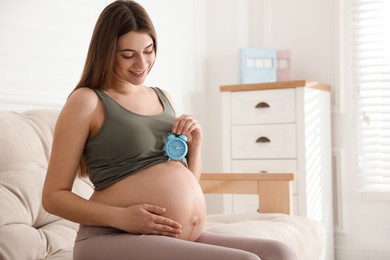 Young pregnant woman holding alarm clock near her belly at home, space for text. Time to give birth