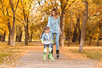 Mother and her daughter roller skating in autumn park