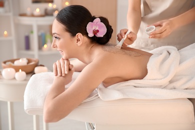 Beautiful young woman having massage with body scrub in spa salon