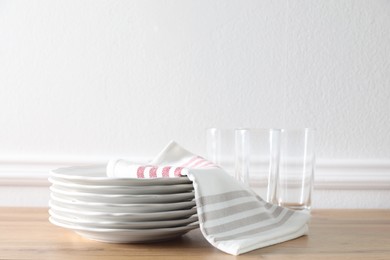 Kitchen towel and clean dishware on wooden table near white wall
