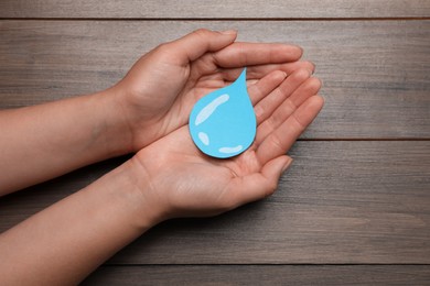 Photo of Save Water concept. Woman holding paper drop at wooden table, top view