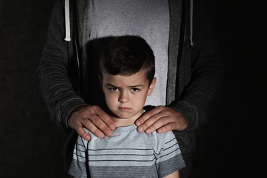 Scared little boy and adult man on dark background. Child in danger