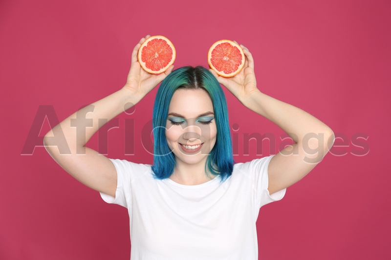 Young woman with bright dyed hair holding grapefruit on pink background