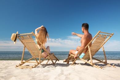 Woman in bikini and her boyfriend on deck chairs at beach. Lovely couple