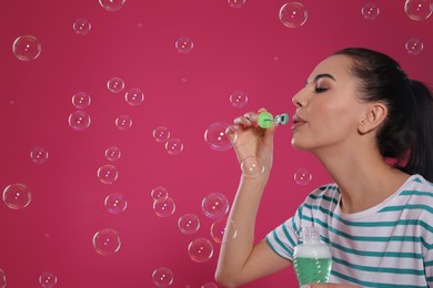 Photo of Young woman blowing soap bubbles on pink background, space for text