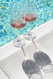 Photo of Glasses of tasty rose wine on swimming pool edge
